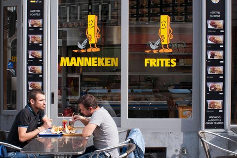 Zwei Männer sitzen vor einer Pommesbude und essen