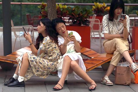 Frauen mit Smartphones sitzen auf einer Bank