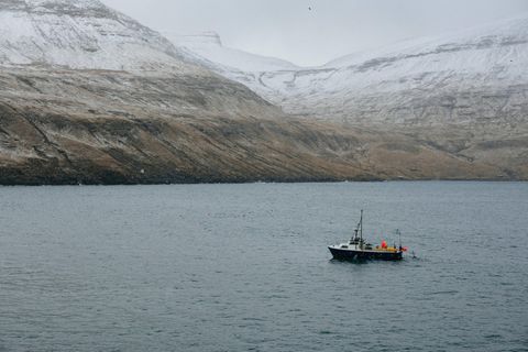 Ein Fischerboot vor verschneiten Bergen der Färöer-Inseln