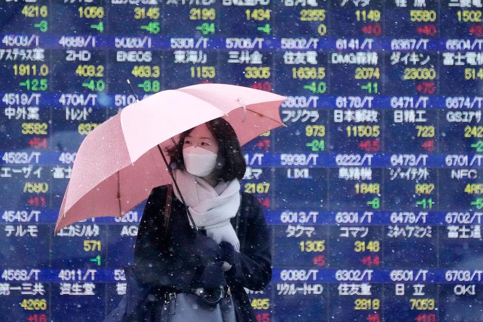Eine Frau mit einem Regenschirm steht vor einem Bildschirm mit Aktienkursen in Tokio