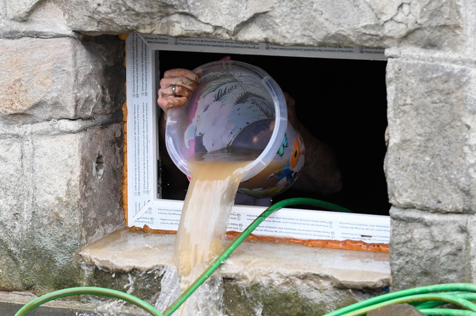 Ein Anwohner beseitigt seine Schäden im Keller, in dem er das Wasser mit einem Eimer aus dem Keller befördert