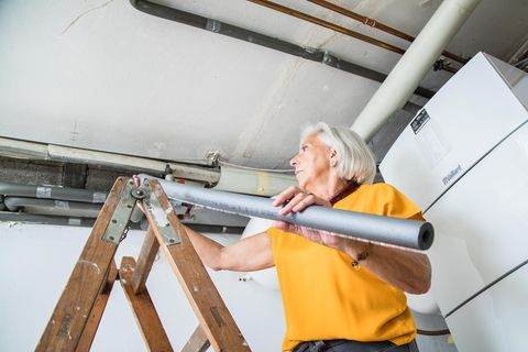 Eine Frau dämmt mit Hilfe eines Isolierschlauchs die Rohre in ihrem Keller