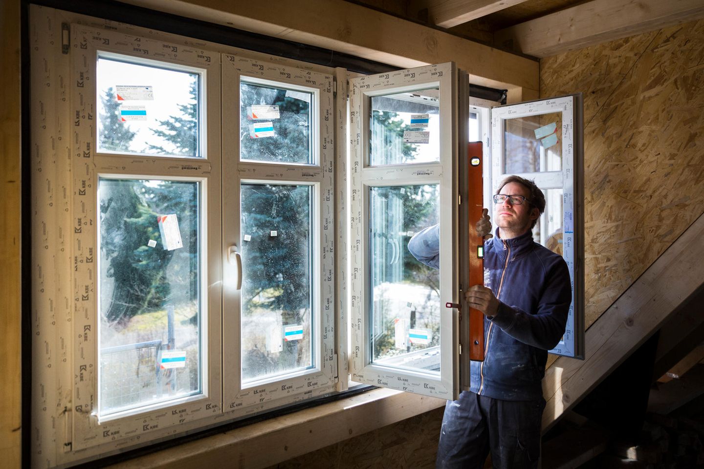Ein Mann kontrolliert auf einer Baustelle mit einer Wasserwaage die Ausrichtung eines neu eingebauten Fensters