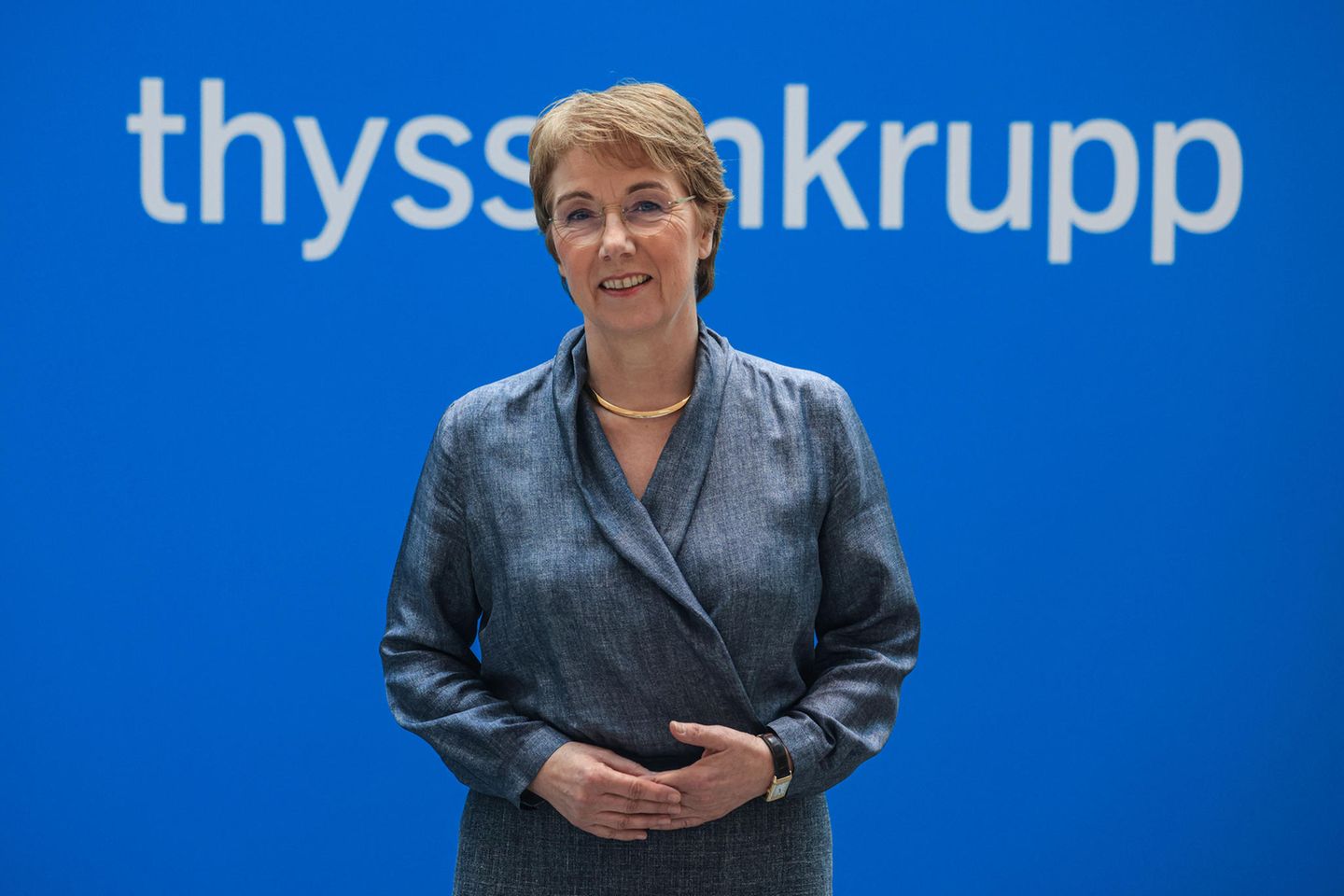 Martina Merz steht vor einer blauen Wand mit dem Schriftzug Thyssenkrupp