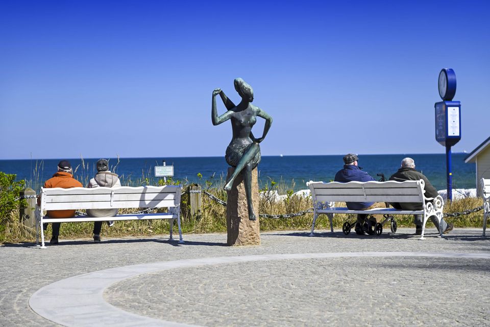 Rentner sitzen auf Bänken und schauen auf die Ostsee