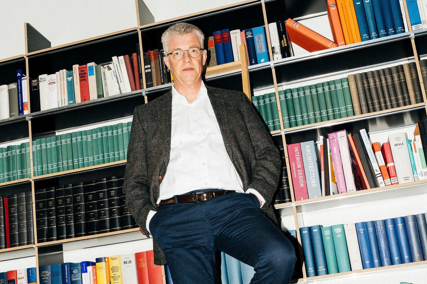 Andreas Koenen steht auf einer Leiter vor einem Bücherregal mit juristischer Fachliteratur