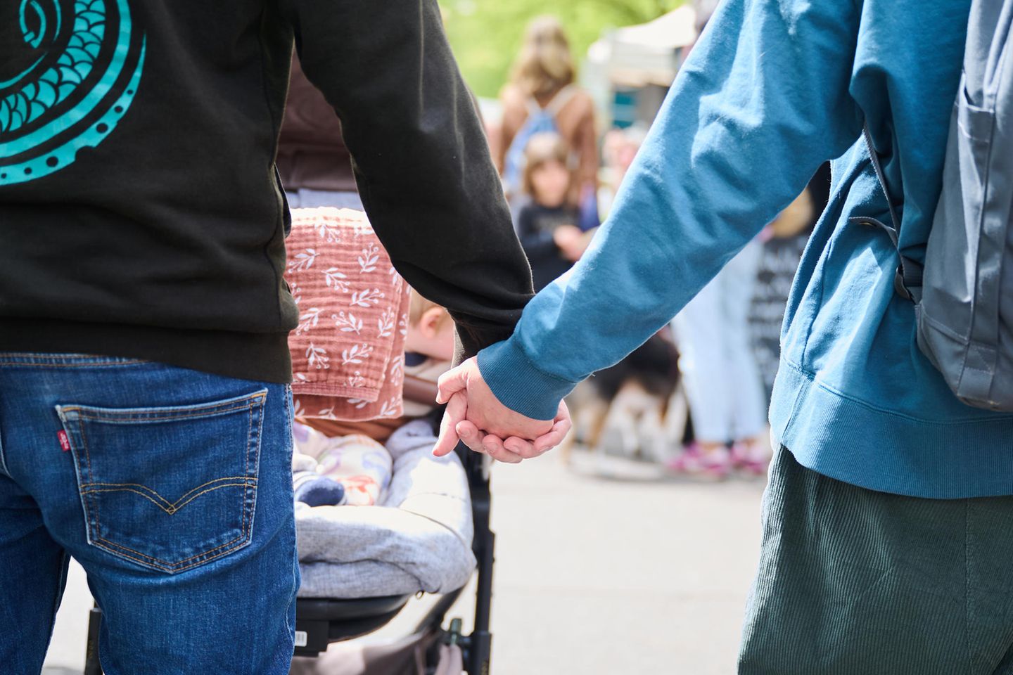 Eltern halten Händchen, während sie mit ihrem Baby im Kinderwagen über einen Markt gehen