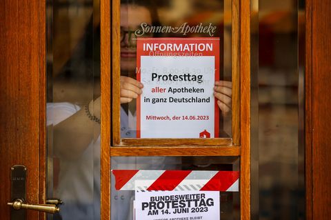 Eine Mitarbeiterin klebt einen Hinweiszettel für den kommenden Schließtag an die Tür der Sonnen-Apotheke