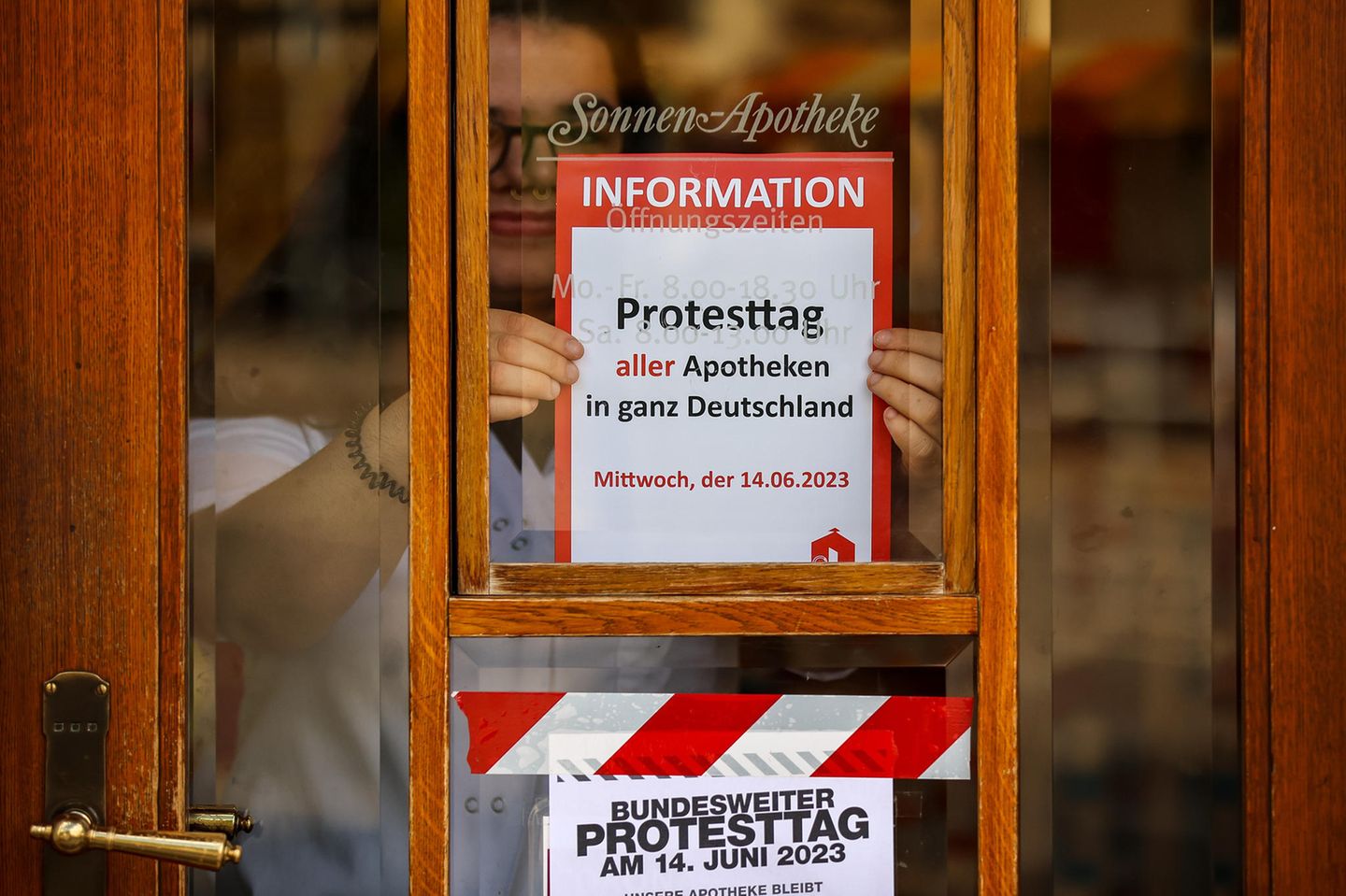 Eine Mitarbeiterin klebt einen Hinweiszettel für den kommenden Schließtag an die Tür der Sonnen-Apotheke
