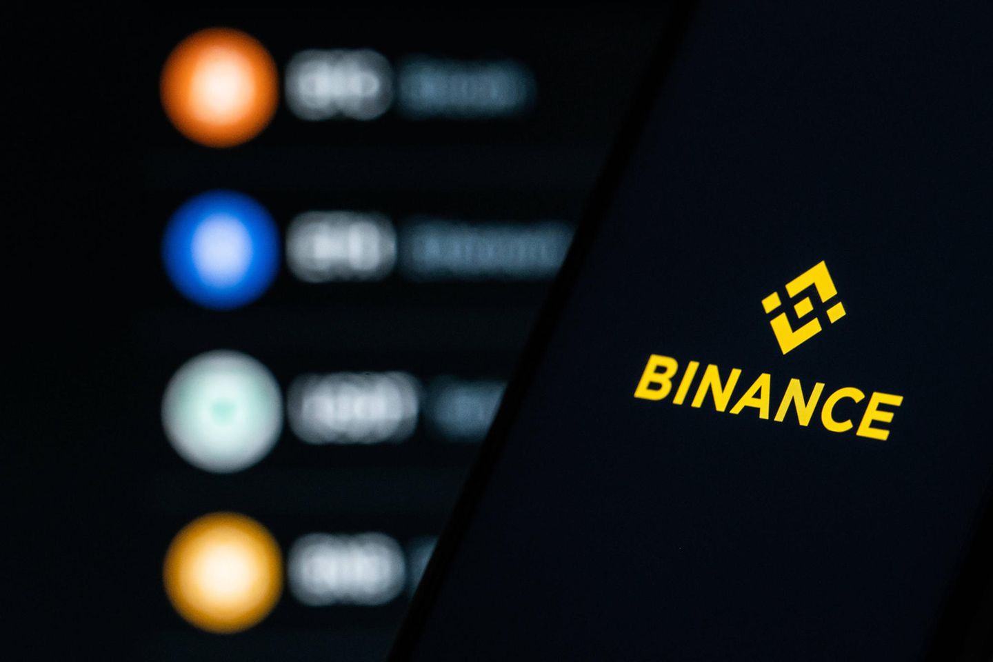 Das Logo der Kryptobörse Binance ist auf einem Smartphone vor einem Bildschirm zu sehen