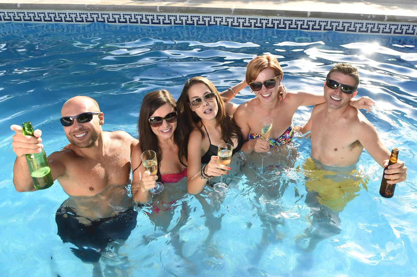 Eine Gruppe junger Leute steht mit Getränken in einem Pool