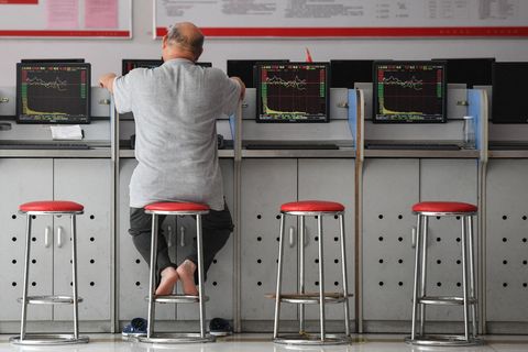Ein chinesischer Anleger sitzt auf einem Stuhl und schaut auf einen Monitor mit Börsenkursen