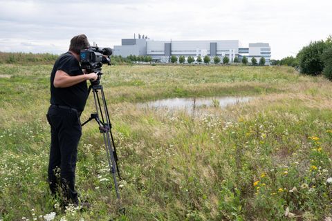 Ein Kameramann steht auf einer Wiese in einem Industriepark im Dresdner Stadtteil Klotzsche