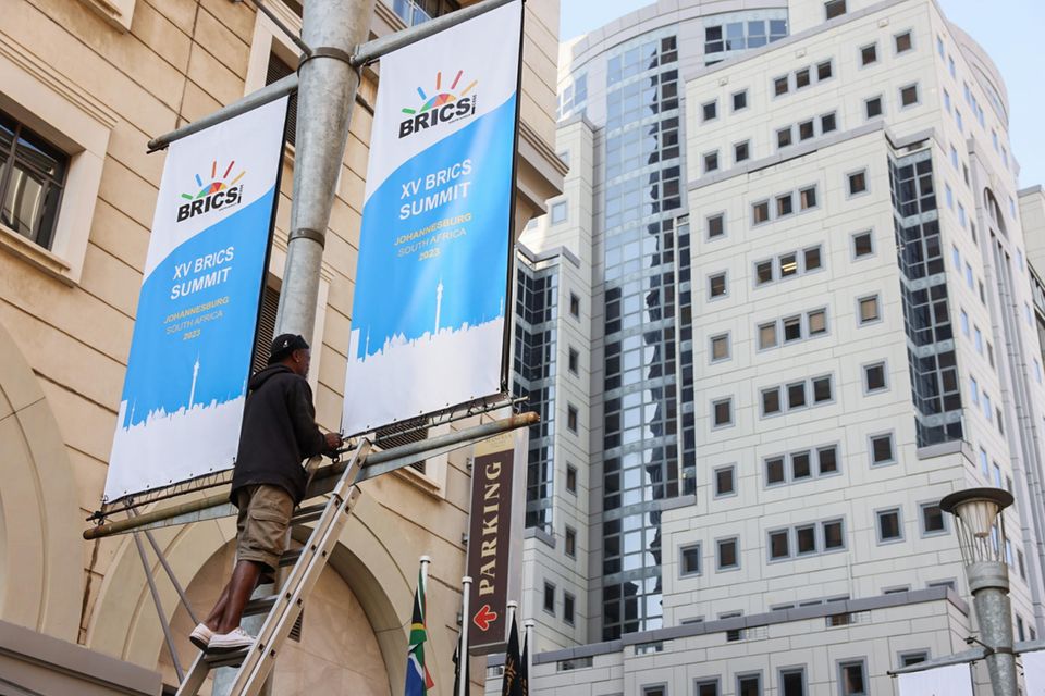 Ein Mann rückt Werbebanner für den BRIC-Gipfel 2023 zurecht, die vor dem Sandton Convention Center aufgehängt wurden