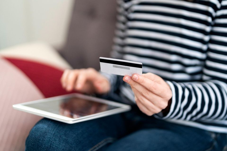 Eine Frau sitzt mit einem Tablet auf den Beinen und hält eine Kreditkarte in der Hand