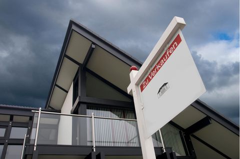 „Zu verkaufen" steht auf einem Schild vor einem modernen Wohnhaus