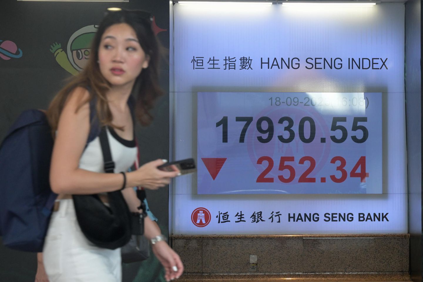 Eine Frau geht an einem Display vorbei, das den Stand des Hang-Seng-Index anzeigt
