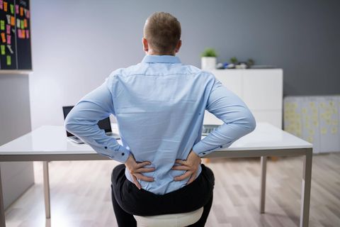 Ein Mann sitzt auf einem Hocker und fasst sich an den Rücken