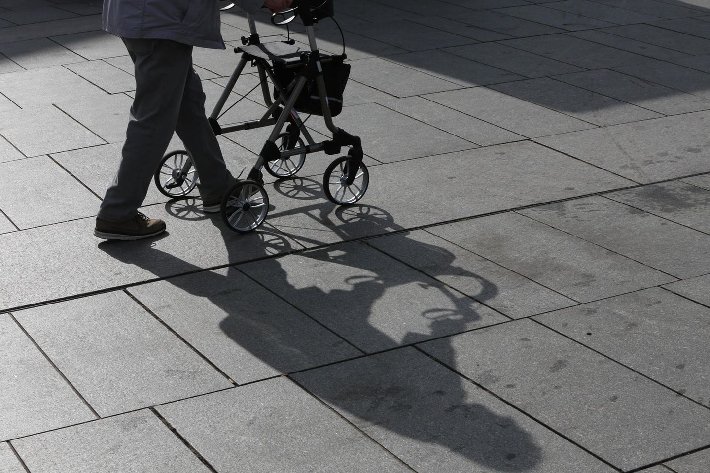 Ein Rentner geht mit einem Rollator über einen Platz