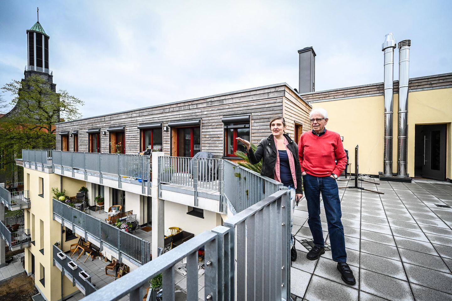 Eine junge Frau und ein älterer Mann stehen auf der Gemeinschaftsterrasse eines Mehrgenerationenhauses