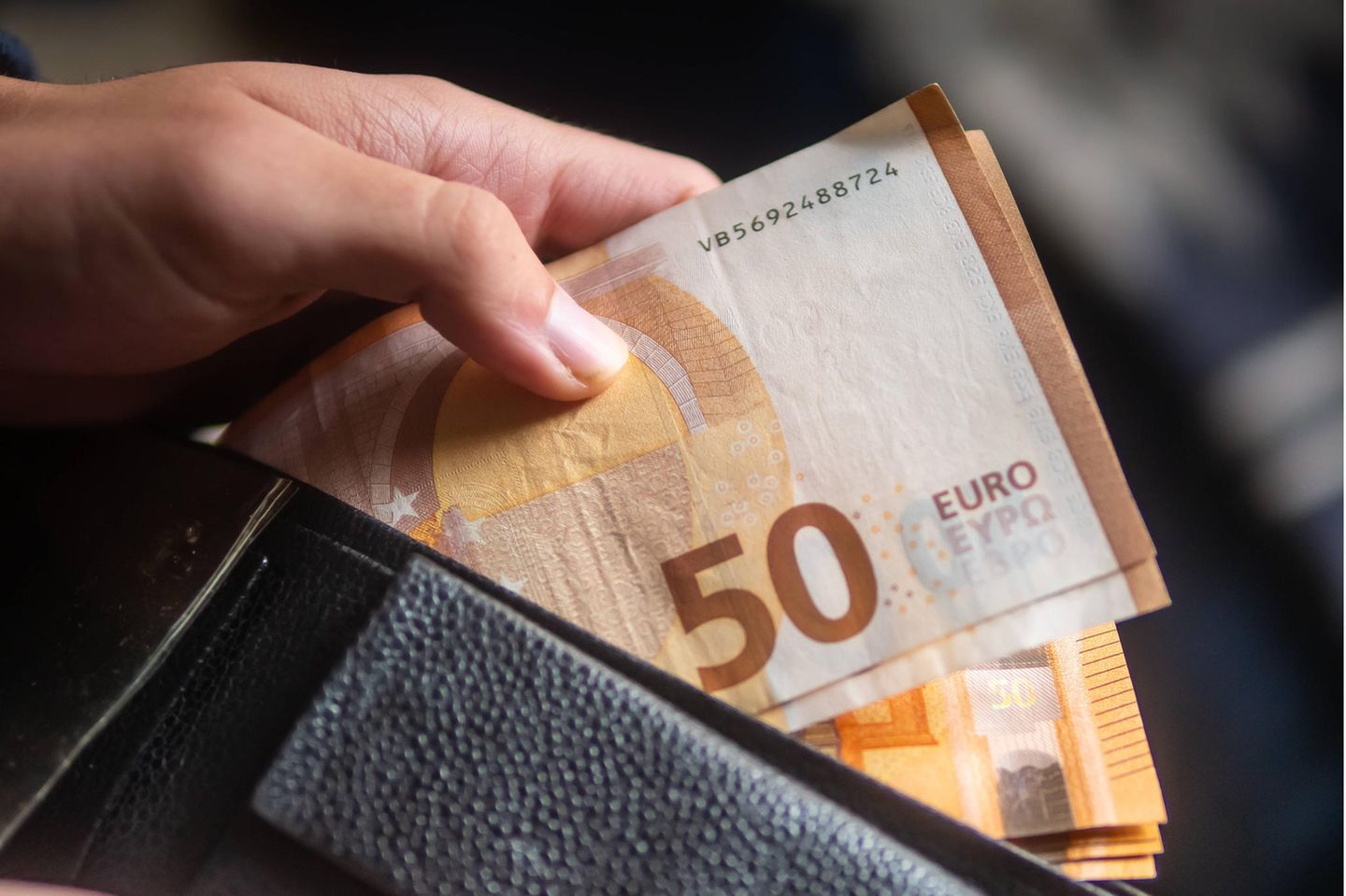 Person zieht Geldscheine aus einer Geldbörse