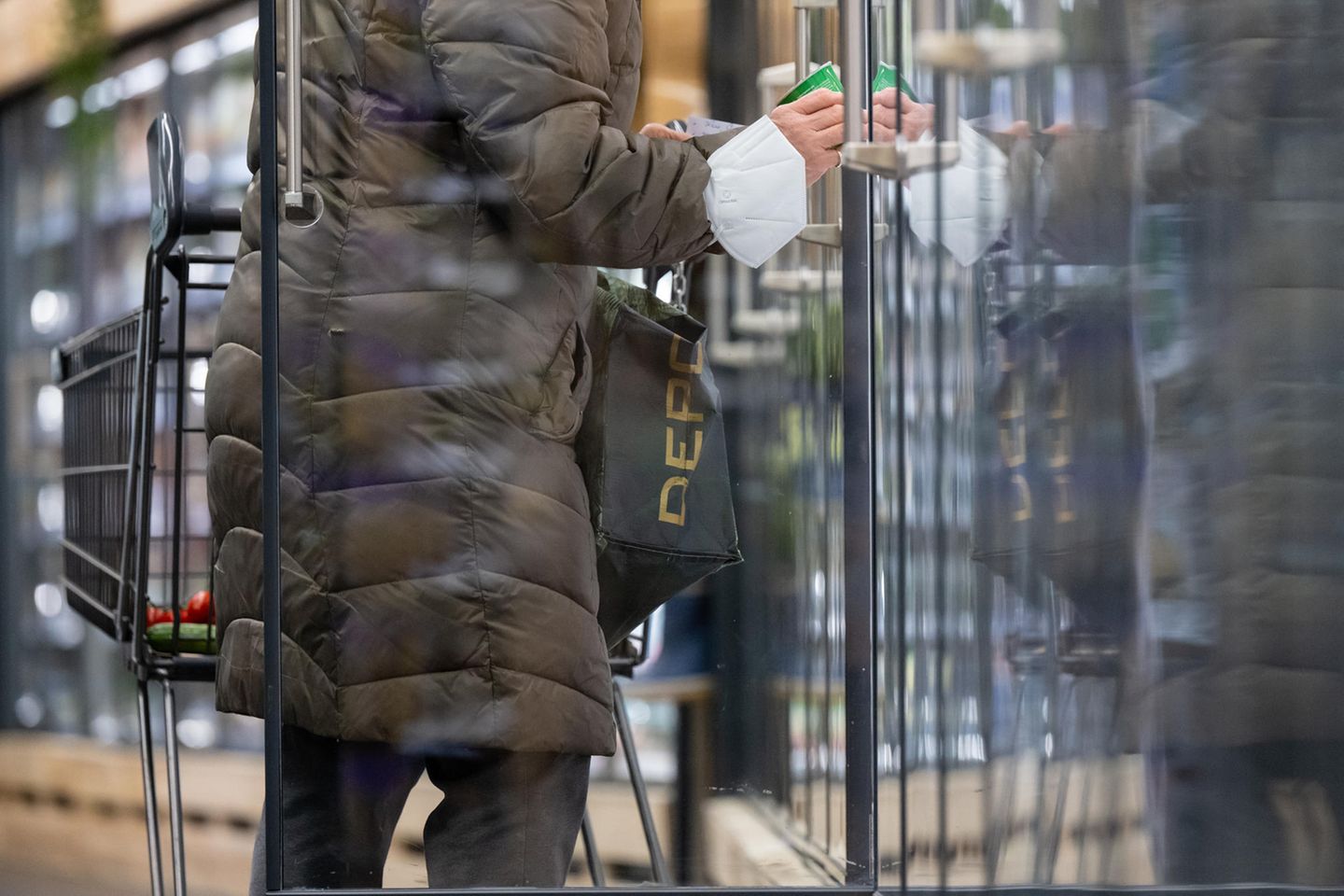 Eine Frau steht mit einem Einkaufswagen in einem Supermarkt an einem Kühlregal