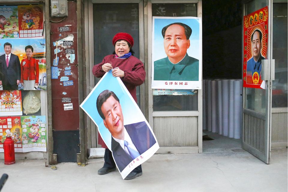 Eine Verkäuferin hält ein Plakat mit dem Konterfei von Xi Jinping, im Hintergrund hängt ein Mao-Plakat
