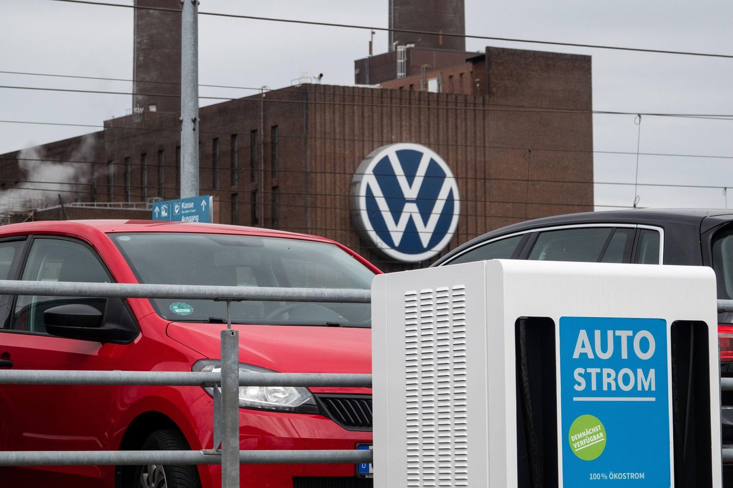 Eine Ladestation für Elektrofahrzeuge steht auf einem Parkplatz, im Hintergrund ist das Volkswagen Werk