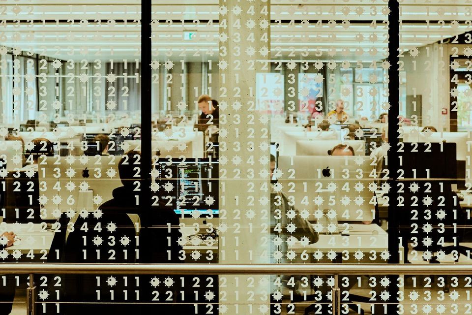 Auf einer Scheibe sind viele Zahlen zu sehen, dahinter ein Raum mit Computerarbeitsplätzen