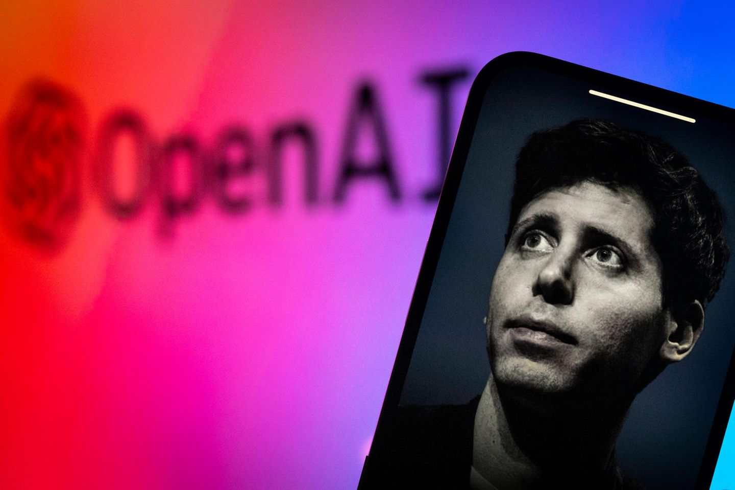 Foto von Sam Altman auf einem Handy-Bildschirm, im Hintergrund der Schriftzug OpenAI