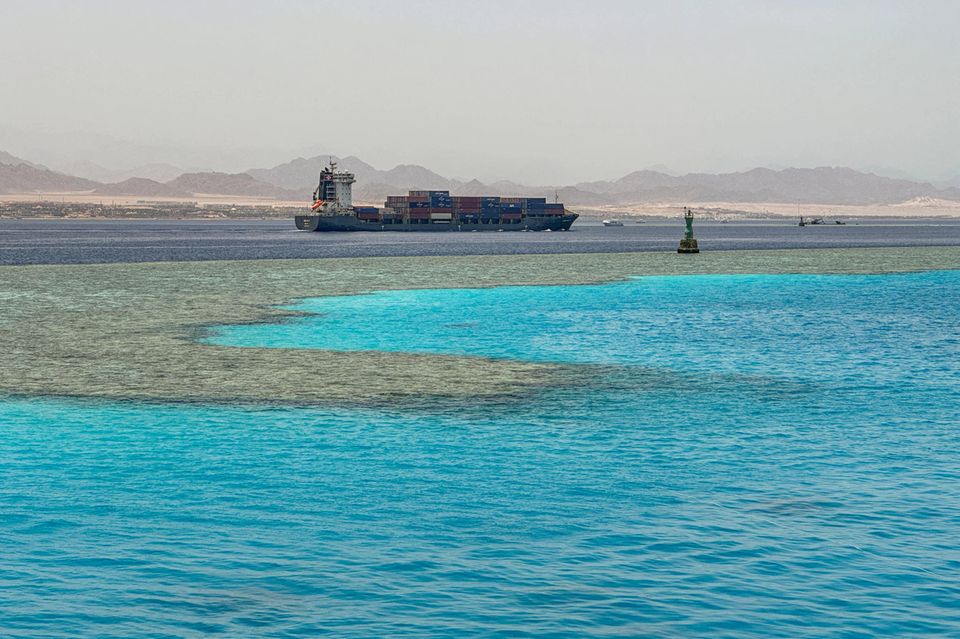 Containerschiff liegt im Meer, im Hintergrund Wüste und Berge