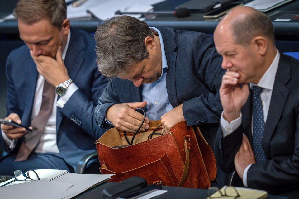 Robert Habeck kramt in seiner Tasche zwischen Christian Lindner und Olaf Scholz