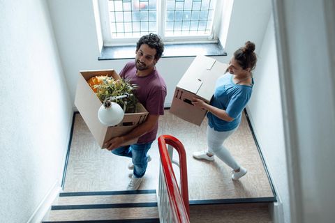 Ein Paar trägt Umzugskisten eine Treppe hoch