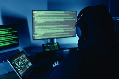 Ein Hacker sitz vor mehreren Computerbildschirmen und führt eine Cyber-Attacke aus