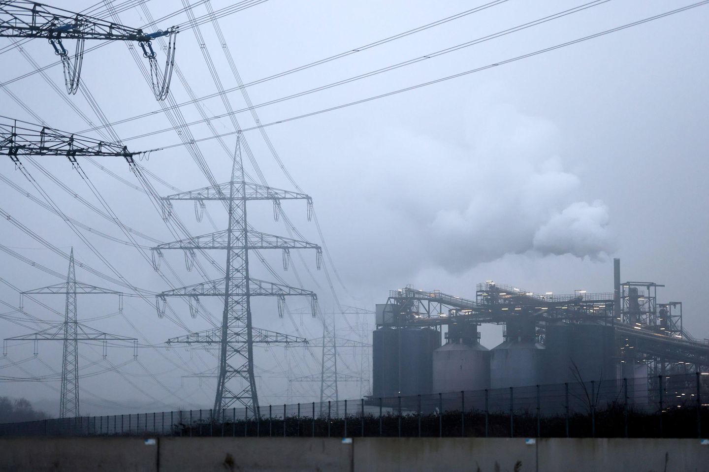 Strommasten stehen auf einem Feld in der Nähe von Industrieanlagen bei Köln