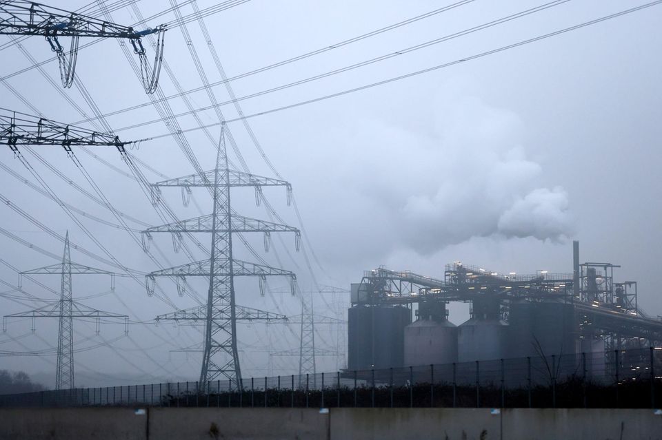 Strommasten stehen auf einem Feld in der Nähe von Industrieanlagen bei Köln