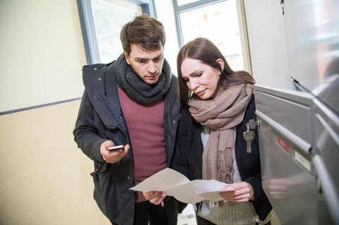 Ein Paar steht in einem Wohnhaus vor einem Briefkasten und liest erschrocken einen Brief