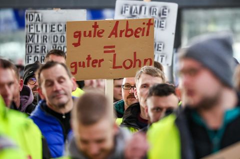 Beschäftigte gehen während eines Warnstreiks mit Schildern „gute Arbeit = guter Lohn“ durch den Flughafen Leipzig/Halle