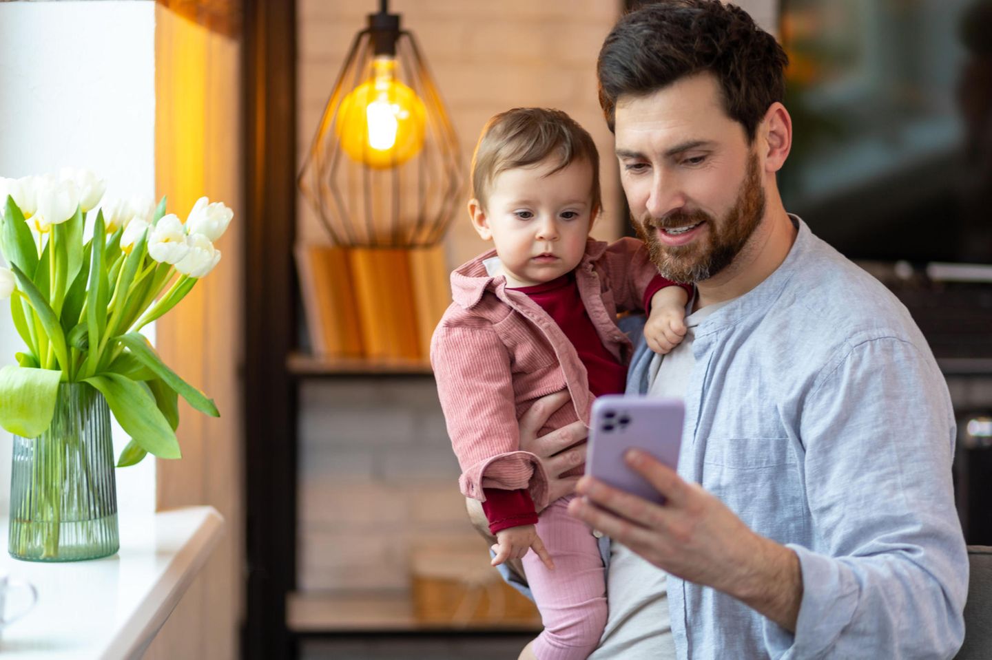 Ein Mann mit einem Kind auf dem Arm und Smartphone in der Hand