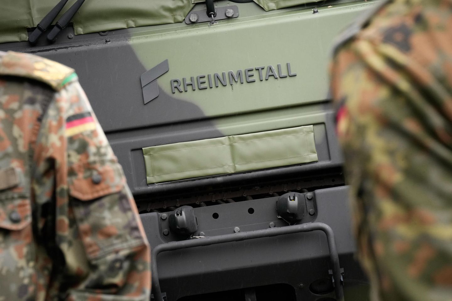 Soldaten der Bundeswehr stehen vor einem Militärfahrzeug in Tarnfarbe und Logo von Rheinmetall