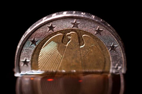 Eine 2-Euro-Münze taucht in eine schwarze Flüssigkeit ein