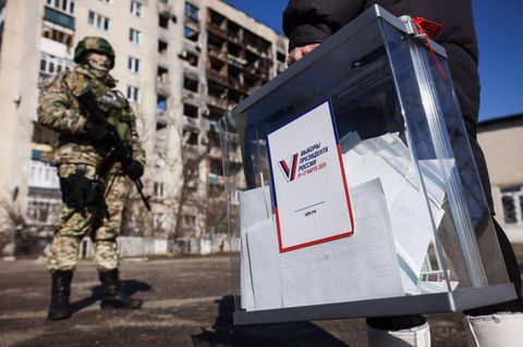 Ein Mann mit einer befüllten Wahlurne läuft an einem bewaffneten russischen Soldaten vorbei