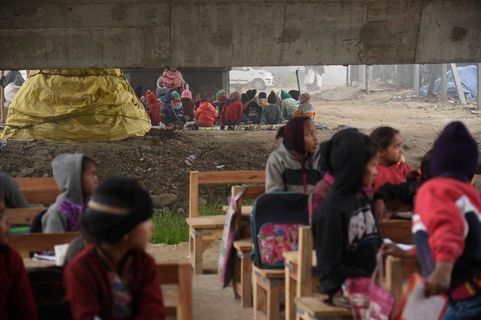 Kinder aus prekärsten Verhältnissen bekommen Unterricht in einer spendenfinanzierten Schule unter einer Brücke in Neu-Delhi 2021. Die indische Schulbildung ist ein ungelöstes Problem. Wohl gehen fast alle Kinder zur Schule, aber die Lehrergebnisse sind bescheiden. Nach Angaben der NGO Pratham, können nur vier von zehn Zehn- bis Elfjährigen in ländlichen Gebieten einen Text lesen, der für die zweite Klasse geschrieben ist. 2005 lag dieser Anteil bei 53 Prozent. Das Ergebnis verschlechterte sich noch durch Covid-19, aber vieles wird pädagogisch veralteten Methoden zugeschrieben, die für Kinder aus bildungsfernen Schichten besonders ungeeignet sind. 