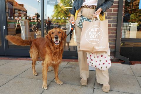 Eine Frau mit einer Einkaufstasche und einem Hund steht vor einer Amazon Fresh-Filiale in Großbritannien