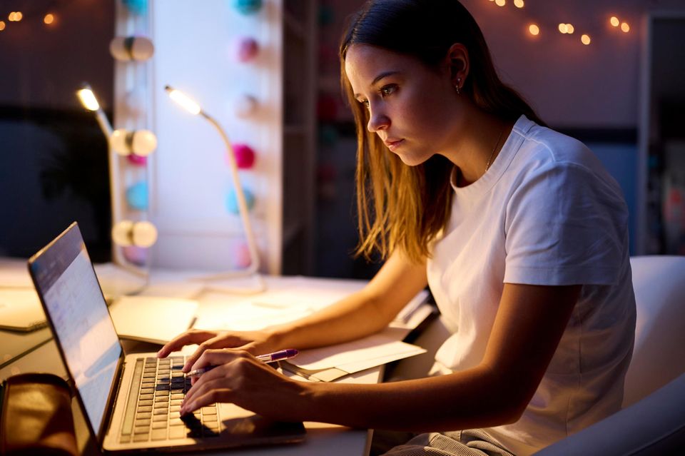 Eine Frau macht Überstunden und arbeitet abends vor ihrem Laptop