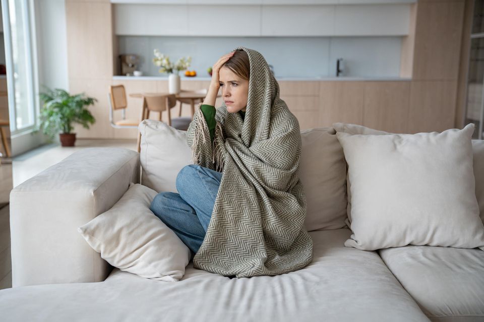 Eine Frau mit Burn-out sitzt in einer Decke gehüllt auf einem Sofa