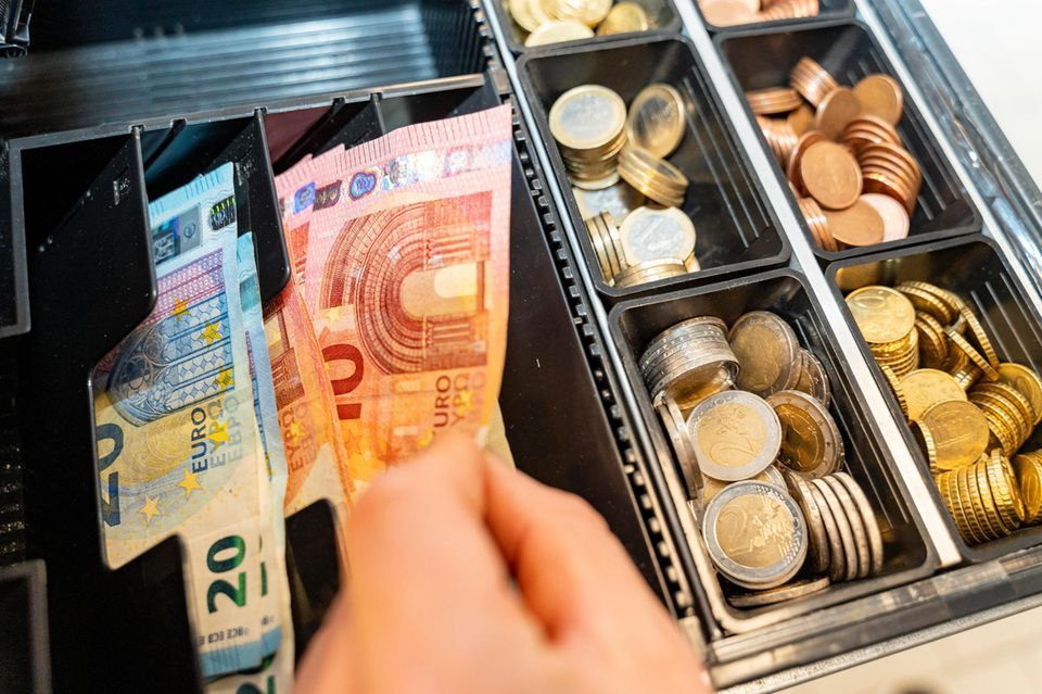 Eine Hand greift nach einem Euro Geldschein in einer Kasse