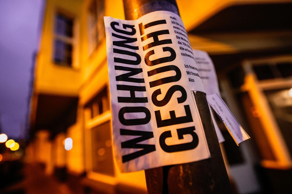 Ein Zettel mit der Aufschrift „Wohnung gesucht“ hängt vor Wohnhäusern