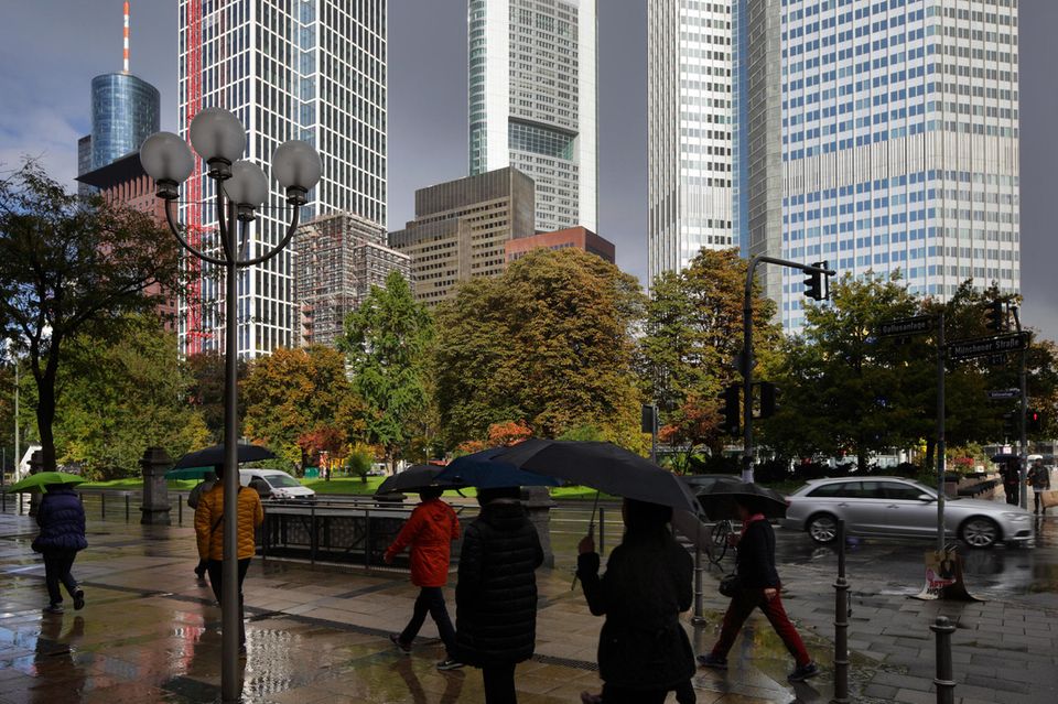 Passanten mit Regenschirmen vor den Bankentürmen Frankfurts