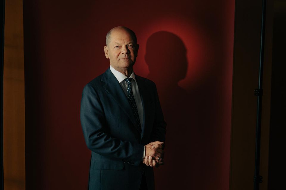 Portrait von Olaf Scholz vor rotem Hintergrund mit gefalteten Händen